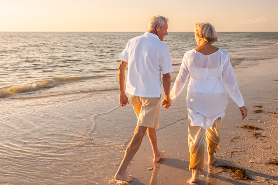 Casal idoso caminhando na praia — vida ativa recuperada após a cirurgia de catarata.